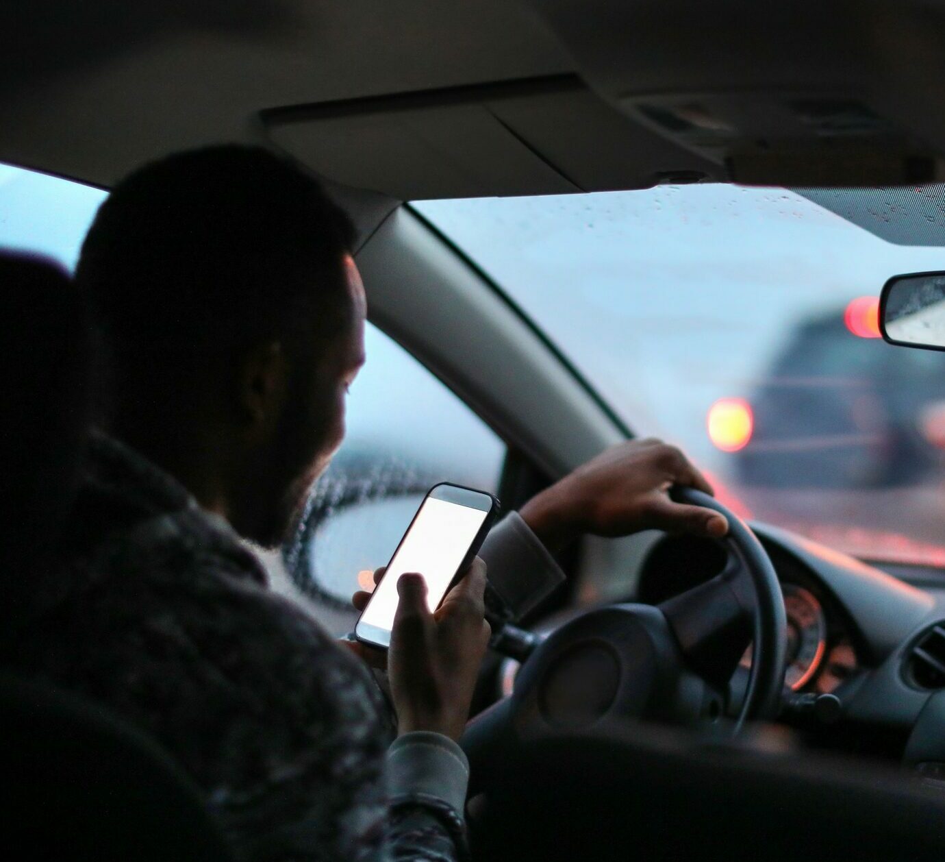 Man using his phone while driving in the rain.