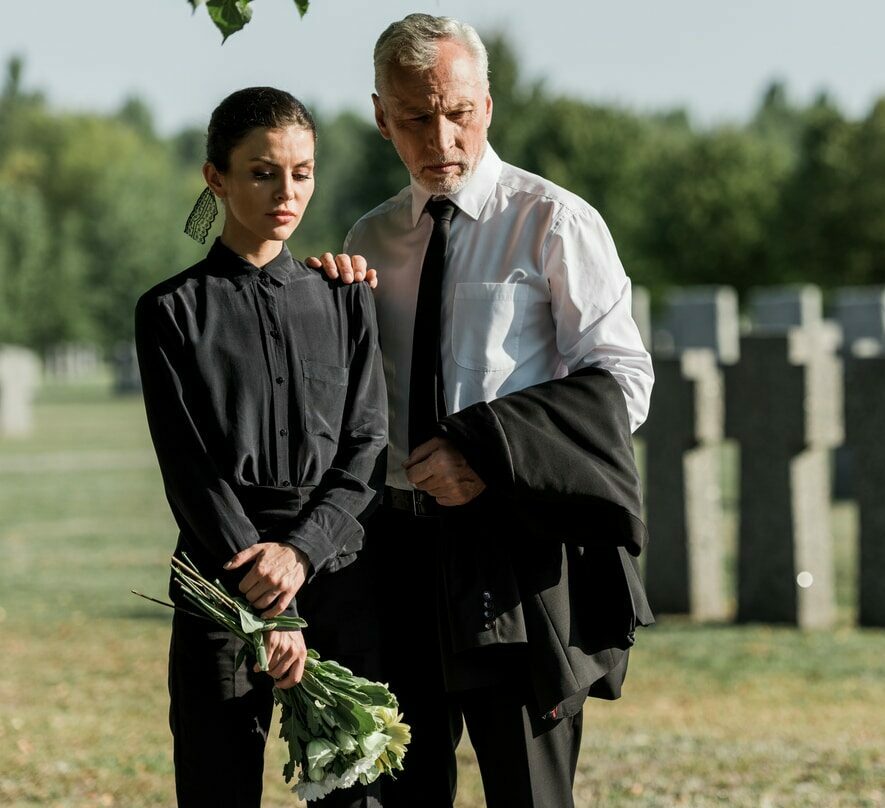 senior man standing with a woman holding flowers on funeral