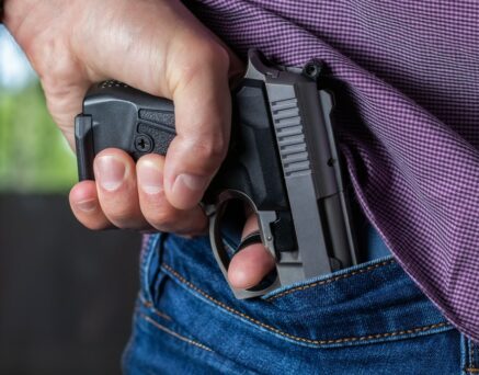 A man holding a gun in his hand behind his back, close-up view. Concepts: crime, attempted murder, a gunshot wound