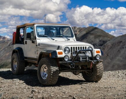 An off-road vehicle stands on a rocky terrain, overlooking a scenic mountainous landscape
