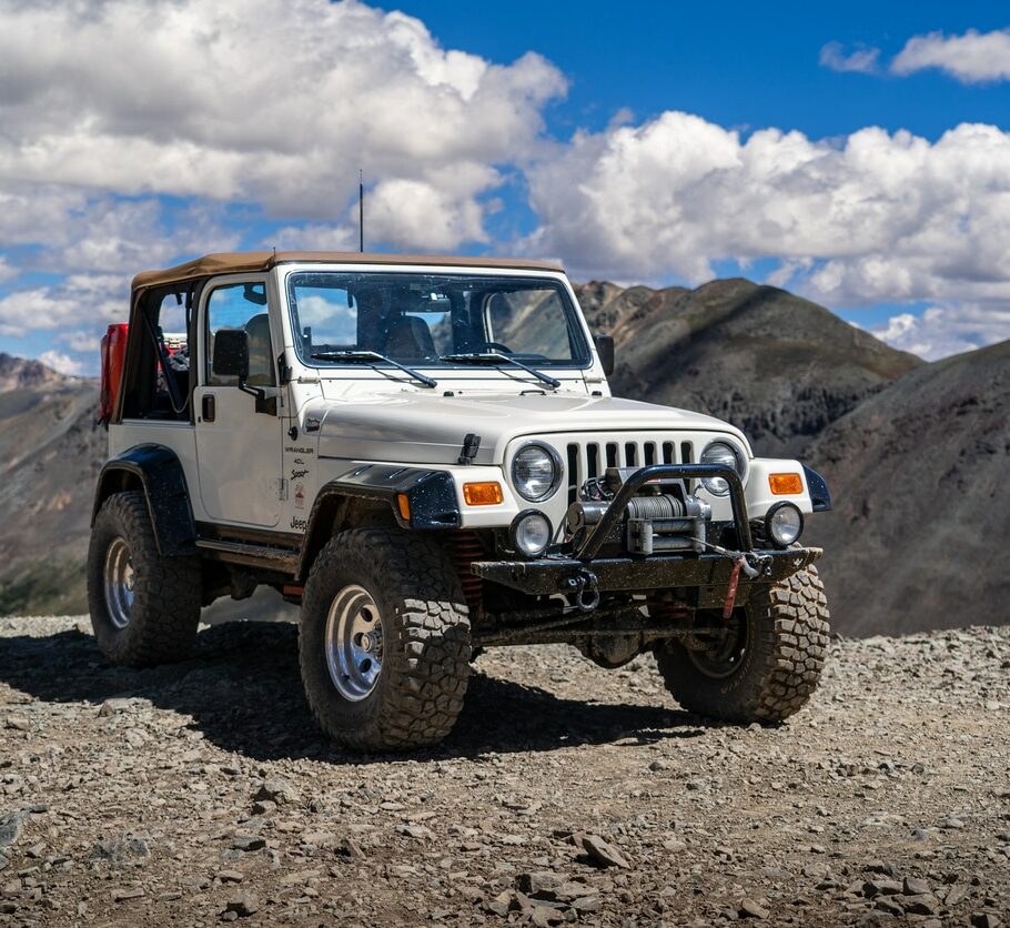 An off-road vehicle stands on a rocky terrain, overlooking a scenic mountainous landscape