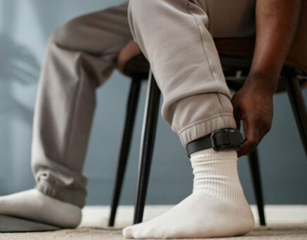 man sitting indoors adjusting electronic ankle monitor on leg