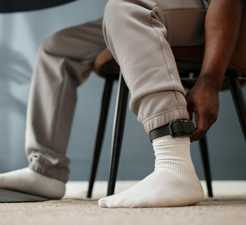 man sitting indoors adjusting electronic ankle monitor on leg