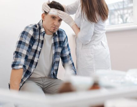 man sitting on the medical bed and receiving the first aid while having the forehead wound